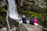 Amigas turistas sentadas en una gran roca, admirando cascada en bosque patagónico