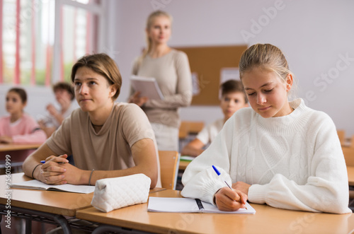 Pupils write in notebooks while sitting at desks in a school class
