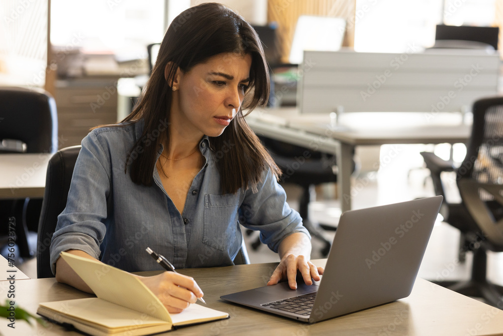 Businesswoman looking focused while taking notes and using a computer Businesswoman looking focused while taking notes and using a computer