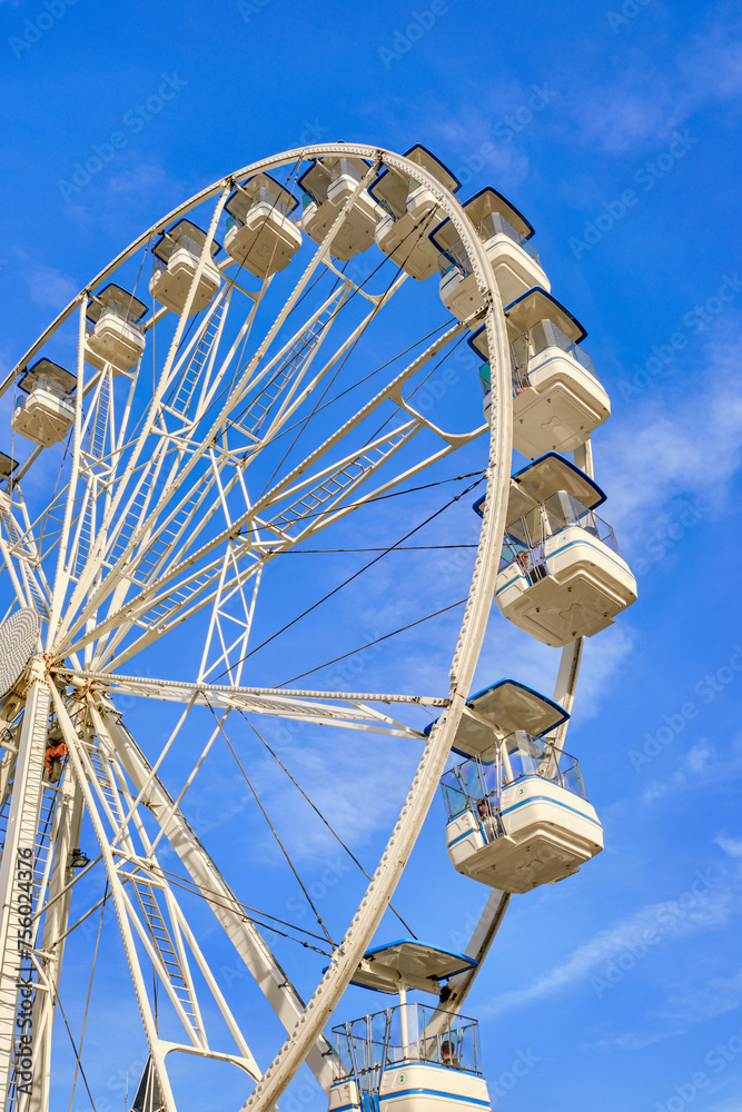 White Ferris wheel on sunny day and clear blue sky with clouds