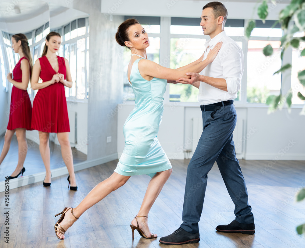 In spacious choreography studio, confident woman professional tango instructor and male student executing dance sequence while young female partner watching intently..