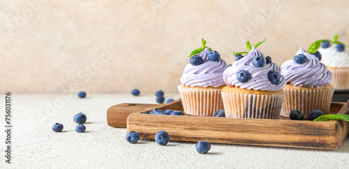 Fotografie Wooden board of delicious cupcakes with blueberries and mint on white background
