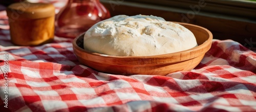 A mixing bowl filled with dough is set on a checkered tablecloth, showcasing a traditional comfort food recipe. The wooden tableware and patterned cloth add a charming touch to the dairyrich cuisine photo