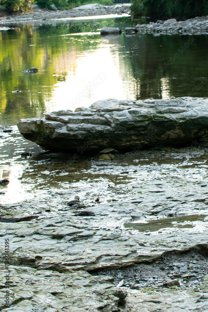 Fototapeta premium A large stone at the bank of a creek that has an evening sunset reflection shining from the water. 