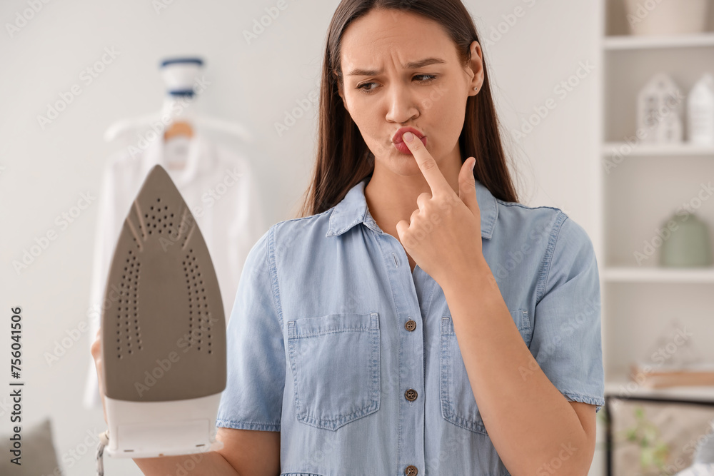Pretty young woman with burnt finger holding hot iron at home Pretty young woman with burnt finger holding hot iron at home