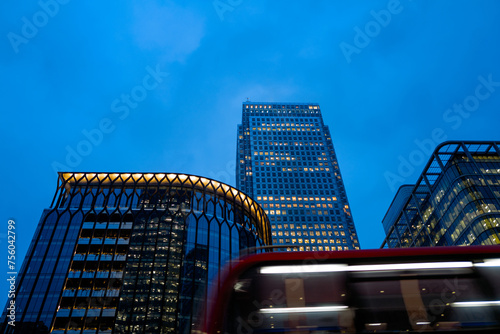 Red Double Decker bus passes city towers at dusk 