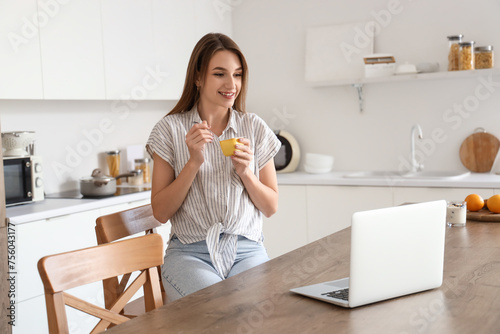 Young woman with tasty yoghurt and laptop in kitchen