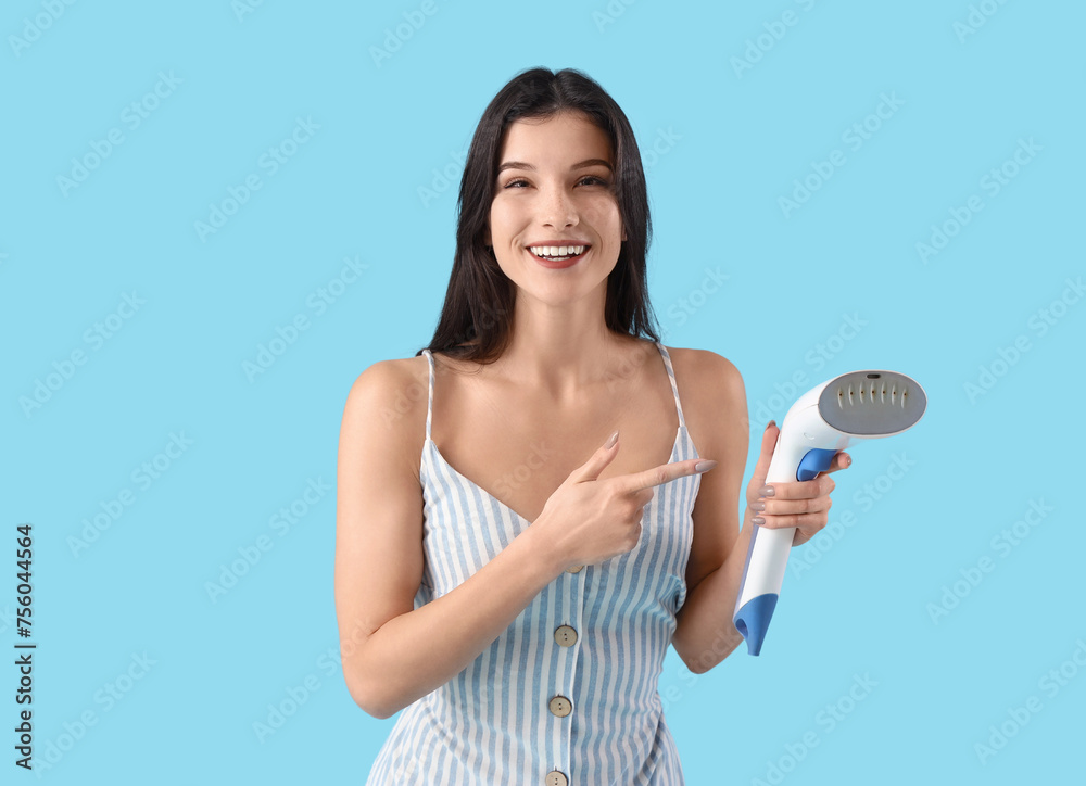 Pretty young woman pointing at modern garment steamer on blue background Pretty young woman pointing at modern garment steamer on blue background