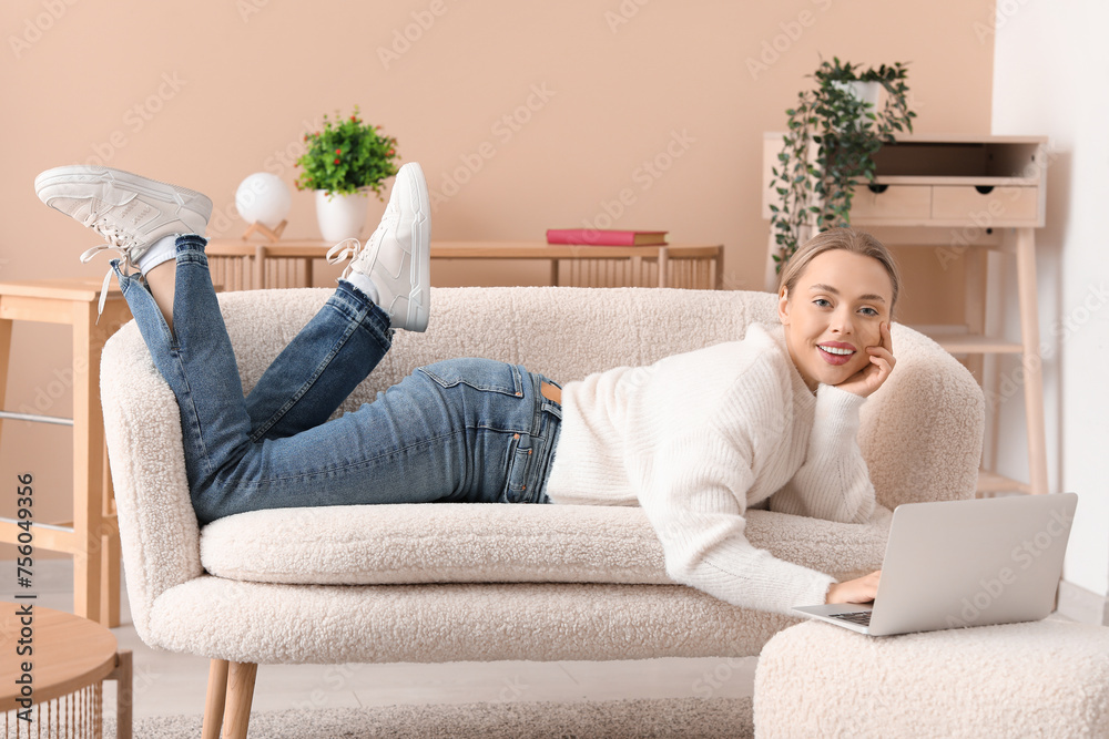 Beautiful young happy woman with laptop lying on comfortable sofa in living room at home Beautiful young happy woman with laptop lying on comfortable sofa in living room at home