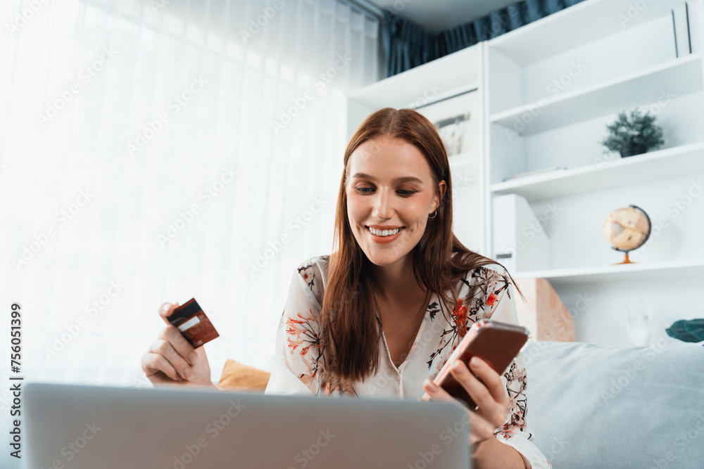 Young happy woman buy product by online shopping at home while ordering items from the internet with credit card online payment system protected by utmost cyber security from online store platform - obrazy, fototapety, plakaty 
