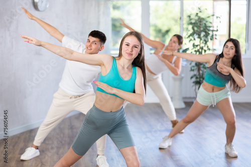 Positive female teenager dances vogue in choreographic school, group of young people in sportswear trains together with their classmates in gym before competitions, battle