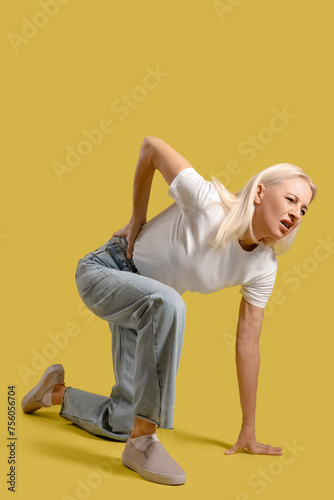 Mature woman suffering from back pain on yellow background