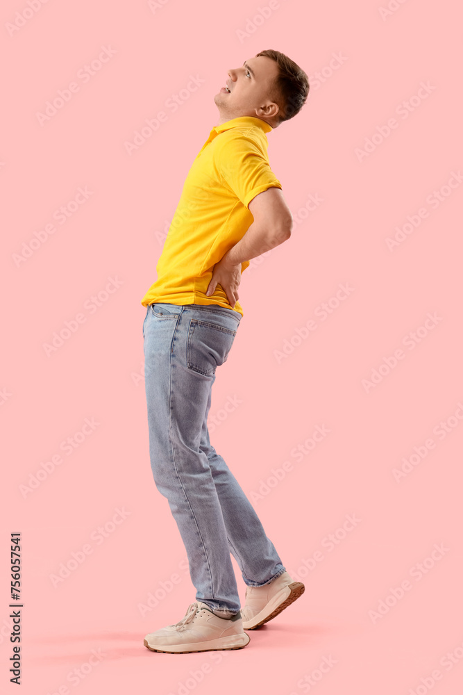 Young man suffering from back pain on pink background