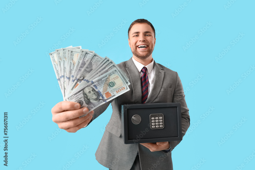 Happy young man with safe box and money on blue background Happy young man with safe box and money on blue background