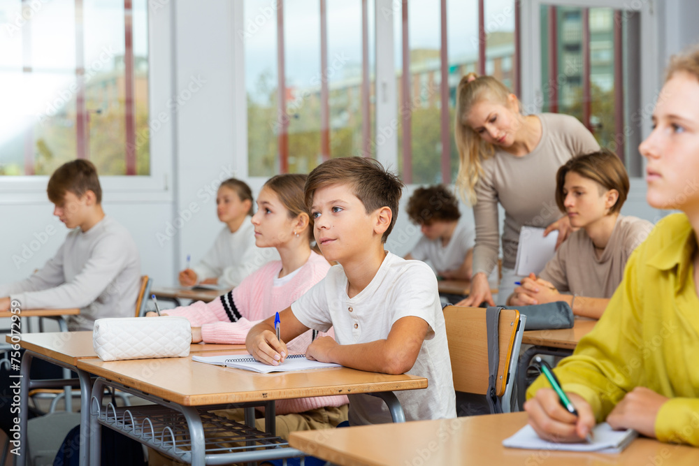 Teen boys and girls sitting at desk in classroom full of pupils during lesson