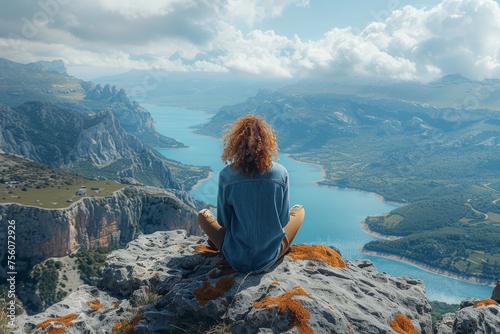 A tranquil scene with a person sitting on a rocky outcrop overlooking a serene blue lake and rugged mountains