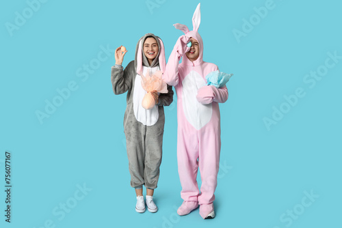 Beautiful young couple in bunny costume with Easter eggs and gifts on blue background