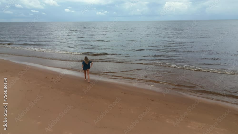Overhead seaside promenade: Aerial view of a woman strolling along a sandy beach near the ocean Overhead seaside promenade: Aerial view of a woman strolling along a sandy beach near the ocean