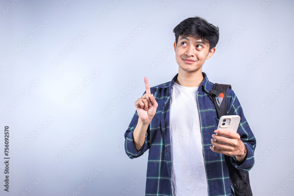 Young Asian college man poiting and looking up to the empty space for ads while holding smartphone Young Asian college man poiting and looking up to the empty space for ads while holding smartphone