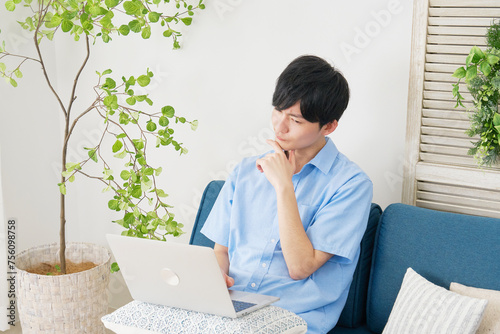 リビングルームで考えながらノートパソコンを使う若い男性