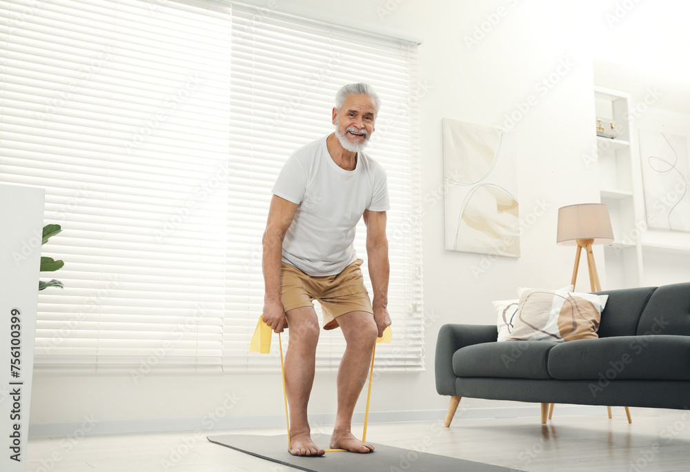 Fototapeta premium Senior man doing exercise with fitness elastic band on mat at home