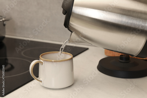 Pouring hot water from electric kettle into cup in kitchen, closeup © New Africa