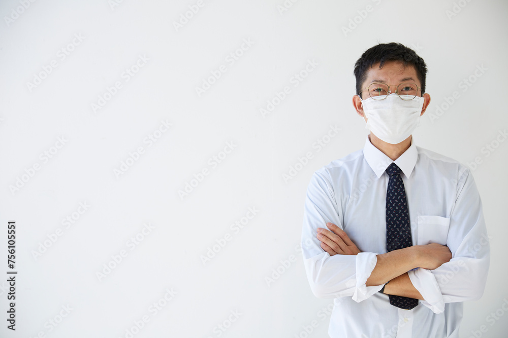 白壁の前でスーツを着てマスクをする男性社員 白壁の前でスーツを着てマスクをする男性社員