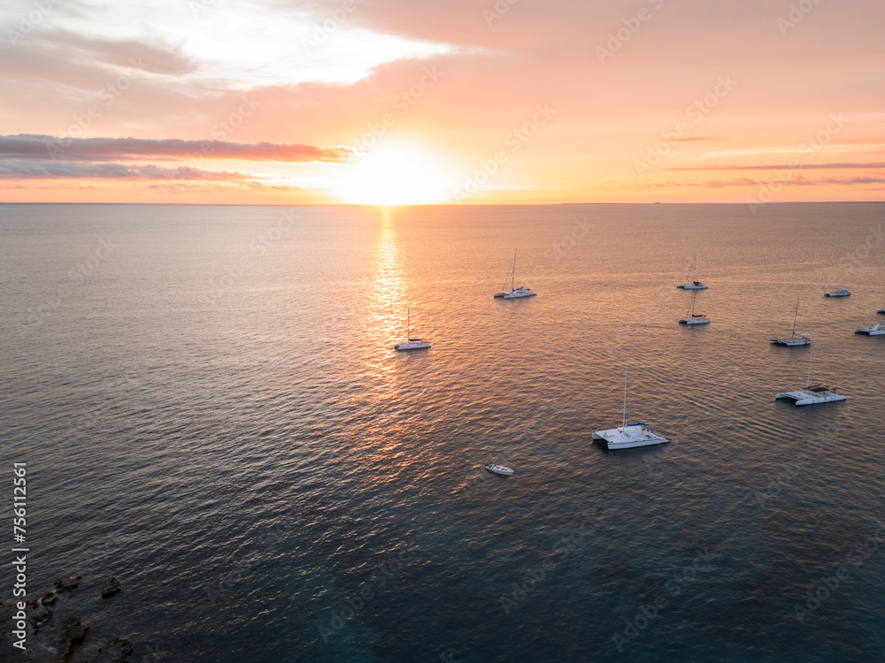 Aerial drone photo of many white yachts and boats at the calm turquoise ocean water shot at sunset hour. South destination, travel, sea navigation concept.