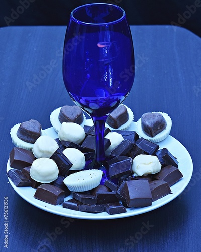 Assorted chocolates placed around a blue wine glass. (ID: 756121936)