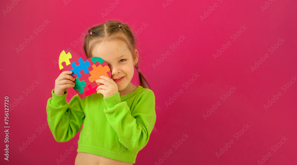 The child shyly covers his face with a heart-shaped postcard made of pieces of cardboard puzzles. Banner in support of people with autism syndrome The child shyly covers his face with a heart-shaped postcard made of pieces of cardboard puzzles. Banner in support of people with autism syndrome