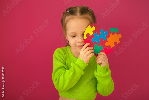 A shy girl hides her face behind a cardboard heart made of multicolored puzzles