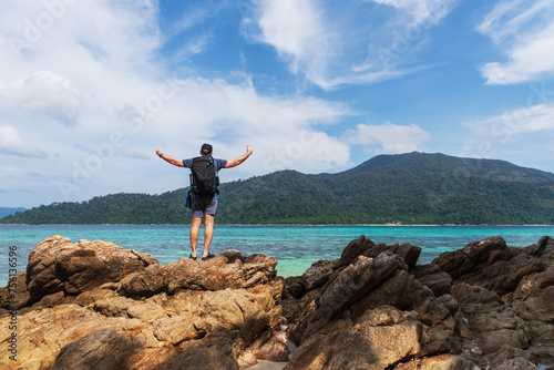 Man tourist with a backpack standing on top of the stone and enjoy the beautiful beach. Travel in Thailand