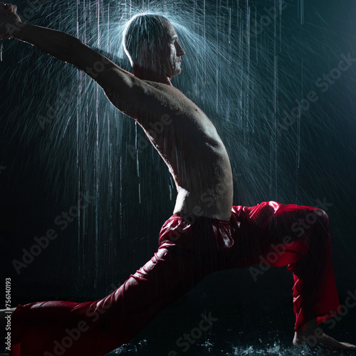 Shirtless man doing yoga under the rain