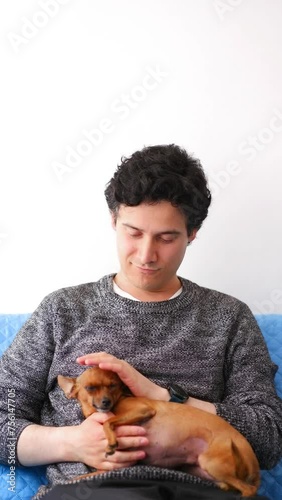Vertical video of Latin man with tousled black hair petting small brown dog