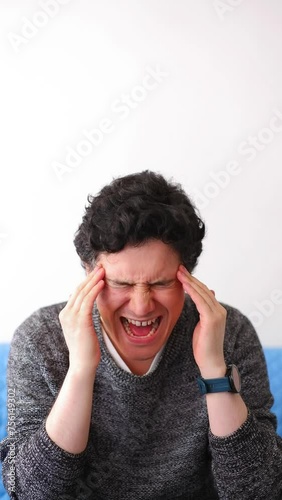 Latino man with messy black hair has a bad headache that he tries to relieve with massages, vertical video