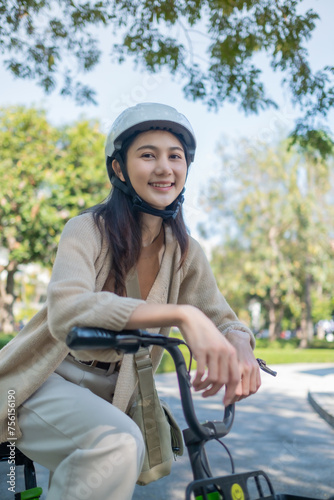 Young beautiful Asian woman in safe bike helmet and protective exercises in riding using electric bicycle in a city park