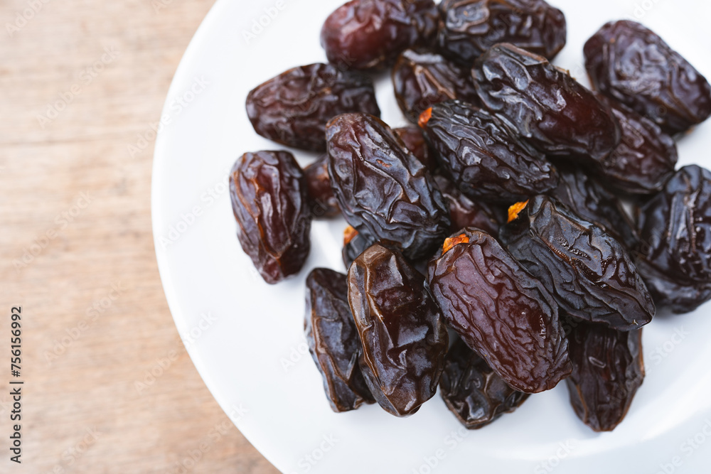 Brown dried Medjool dates in a white plate are sweet and juicy. They are eaten by Muslims during fasting. Brown dried Medjool dates in a white plate are sweet and juicy. They are eaten by Muslims during fasting.