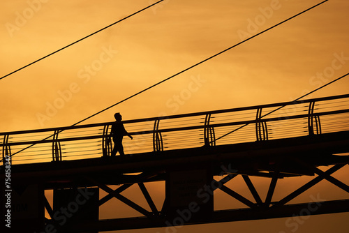 Silhouette person walking at bridge over sunset.