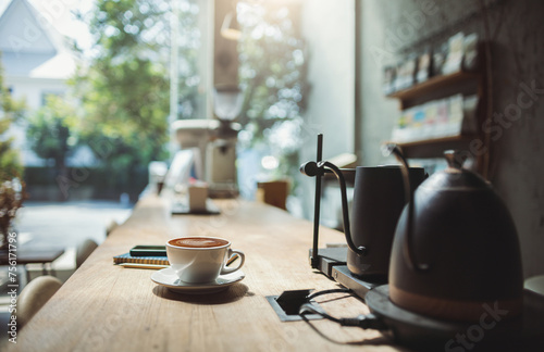 Latte coffee in tea cup with note book and phone on wooden counter in cafe for brakefast