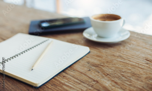 Select focus at pencil on blank note book with coffee cup and mobile on old wooden table