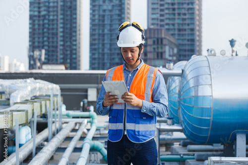 Asian man engineer holding tablet working at rooftop building construction. Male technician worker working checking hvac of office building. Engineering installing large air conditioning system.