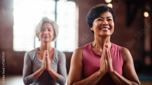 A middle-aged woman with short, elegant hair and a cheerful Asian woman practice yoga poses in the gym.