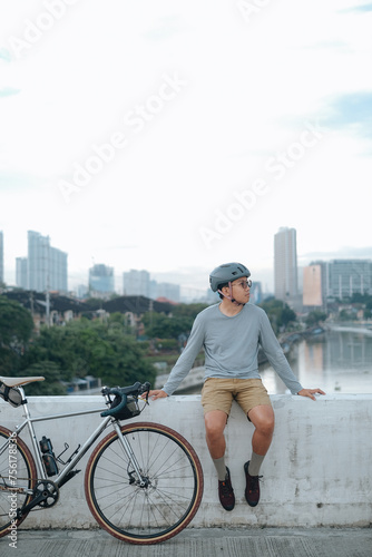Fototapeta Naklejka Na Ścianę i Meble -  A young cyclist sitting on a bridge in the city.