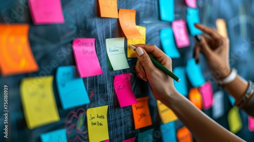A person's hand placing colorful sticky notes on a blackboard, conceptualizing planning and strategy development.