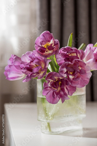A bouquet of pink tulips in a beautiful stylish vase on the table in the room. The concept of the onset of spring and International Women's Day on March 8.