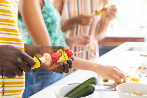 Diverse group of people preparing vegetable skewers in a bright kitchen