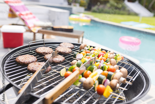 Burgers and vegetable skewers are grilling by a poolside