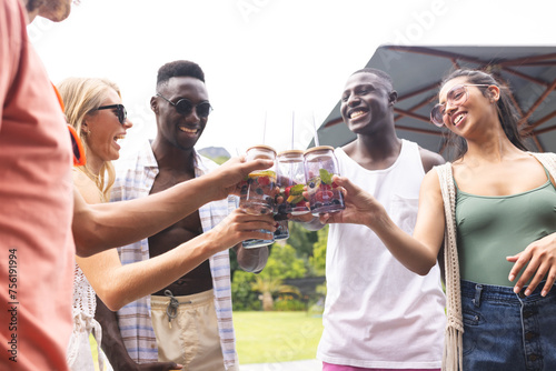 Diverse group of friends toasting with drinks, smiling during an outdoor gathering