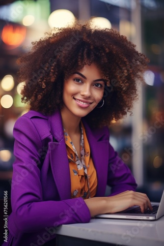 Woman with curly hair is sitting at table with laptop
