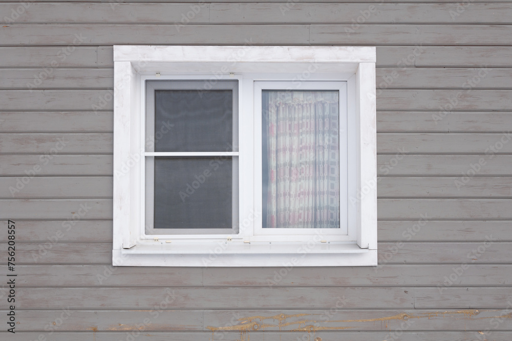 Facade of a wooden house with a white window on a gray wall